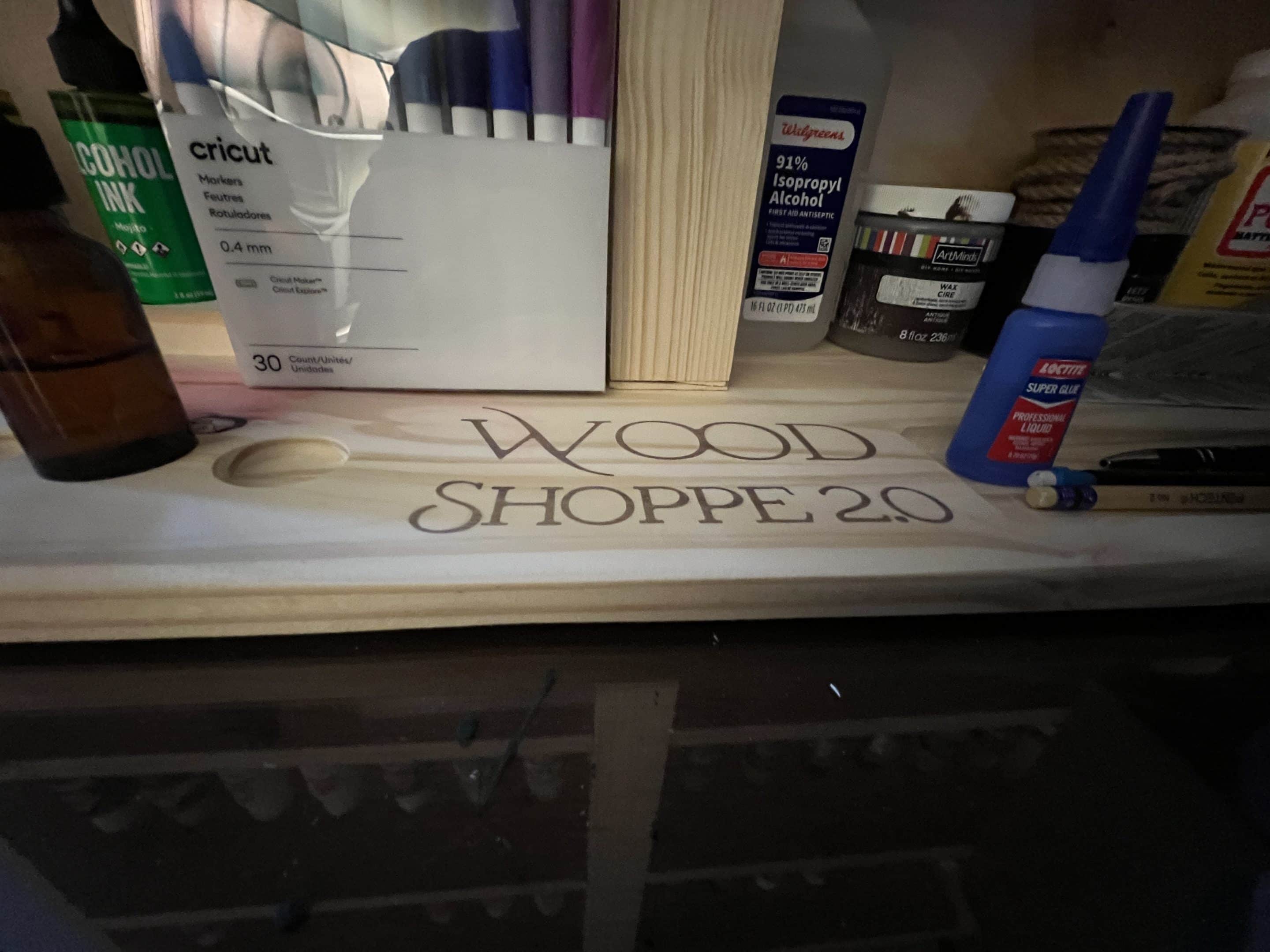 Wood Shoppe 2.0 -- Wooden Inlay CNC-carved Wood Shoppe 2.0 logo engraved into a wooden board, surrounded by workshop tools and supplies.